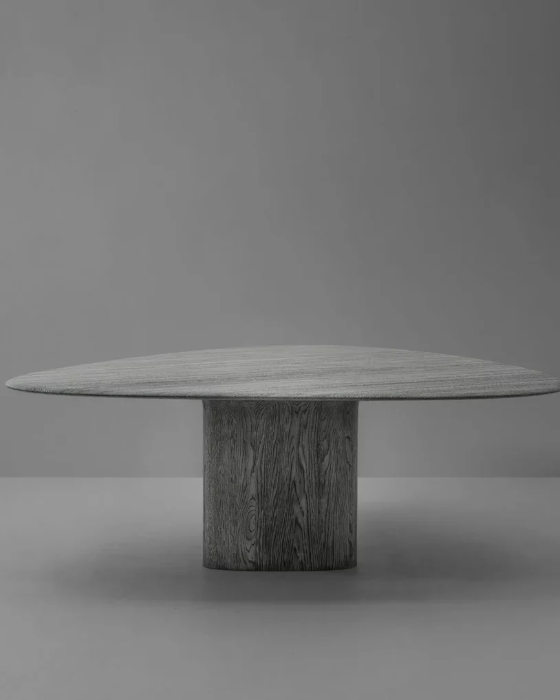 Anvil Dining Table Triangle Van Rossum, ontwerp Pieter Maes, massief houten eettafel in eiken of walnoot met afgerond driehoekig blad en sculpturale basis, verkrijgbaar bij Nuances Leuven