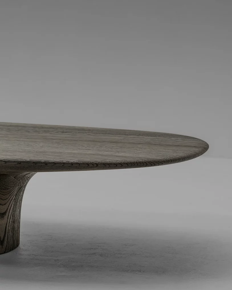 Anvil Coffee Table Van Rossum, ontwerp Pieter Maes, geometrische salontafel in eiken of walnoot met ovaal blad en sculpturale basis, verkrijgbaar bij Nuances Leuven